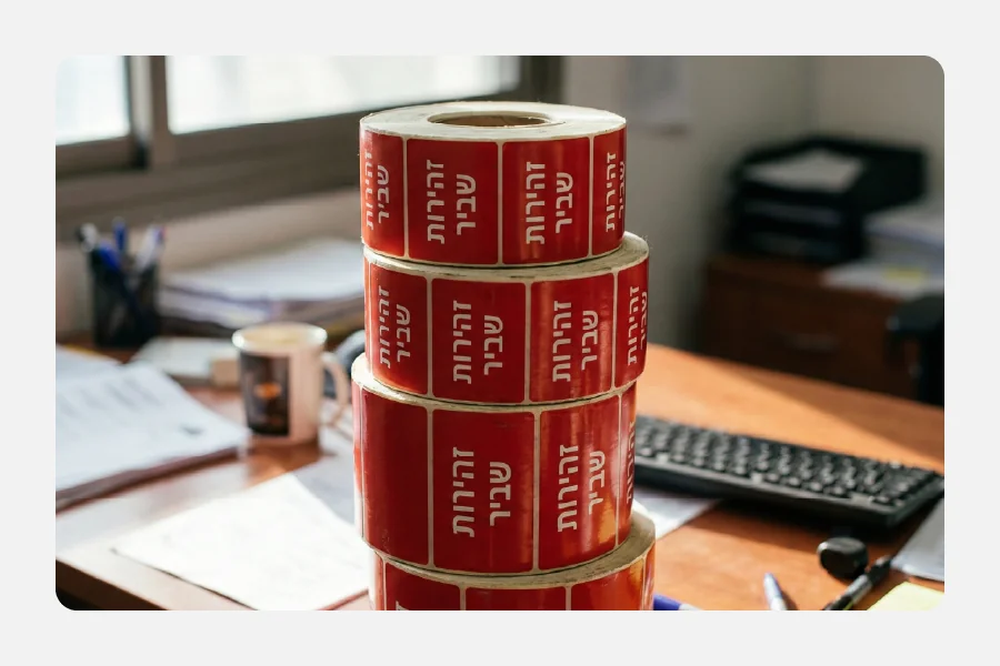 מגדל של גלילי מדבקות אדומות עם כיתוב זהירות שביר בלבן למשלוחים