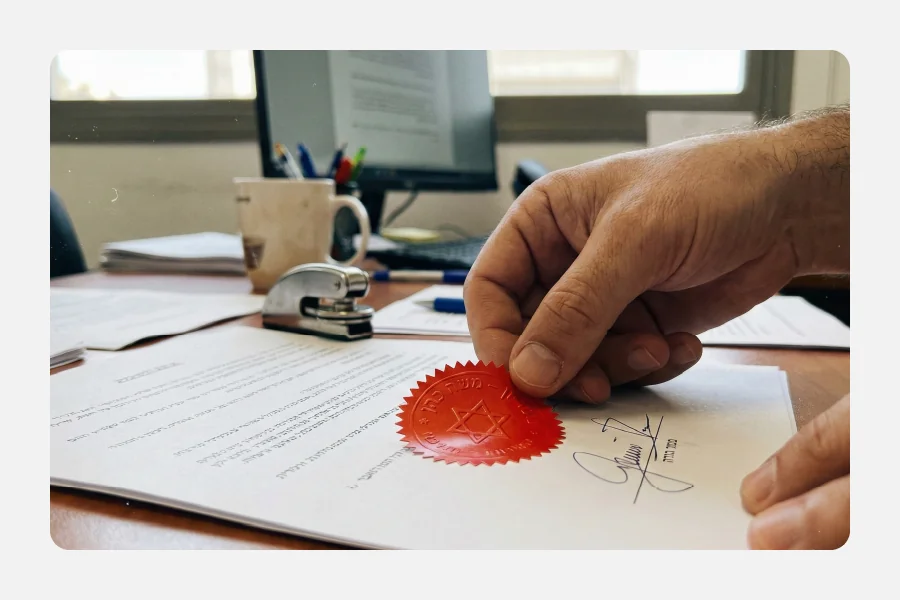 יד מדביקה מדבקת חותם אדום של נוטריון על מסמך חתום במשרד עורכי דין.