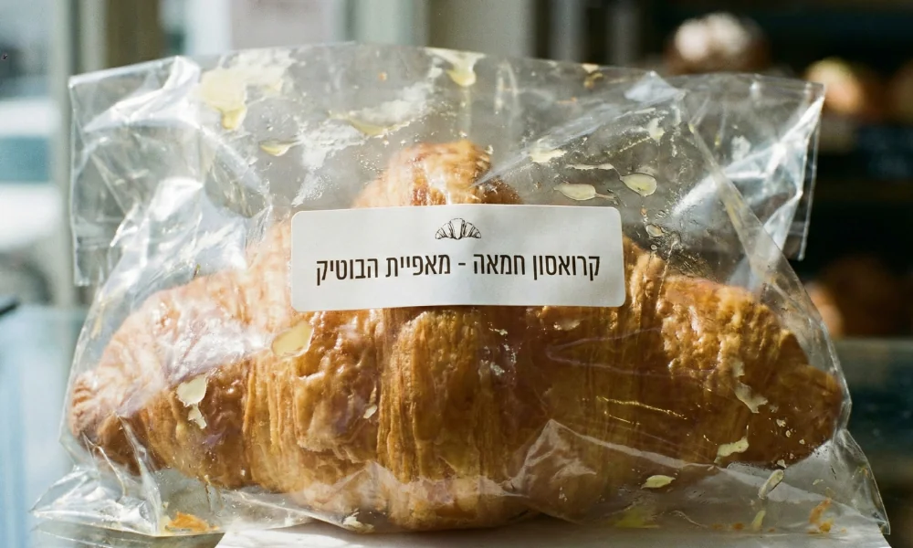 שקית פלסטיק שקופה המכילה קרואסון חמאה עם מדבקה לבנה נקייה "קרואסון חמאה - מאפיית הבוטיק".