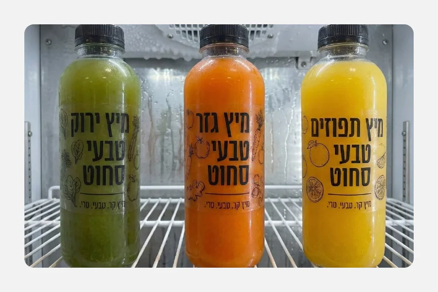 בקבוקי מיץ טבעי במקרר עם מדבקות שקופות ממותגות עם איורי פירות וירקות וכיתוב שחור