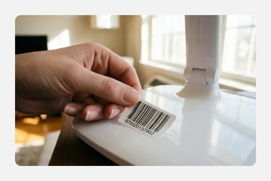 יד מדביקה מדבקת ברקוד ומספר סידורי לבנה על בסיס של מנורה או מוצר חשמלי