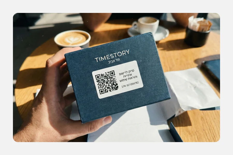 יד מחזיקה קופסת תכשיטים כחולה עם מדבקת QR קוד לרישום אחריות והוראות שימוש.