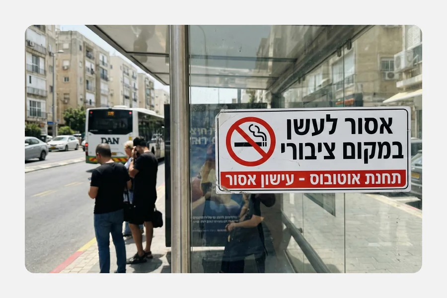 מדבקת ויניל PVC לבנה על זכוכית של תחנת אוטובוס עם תמרור "אסור לעשן במקום ציבורי" וכיתוב בולט באדום ושחור.