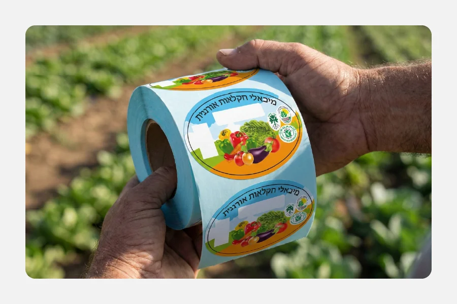 ידיים של חקלאי מחזיקות גליל מדבקות עגולות בצבע תכלת לסימון תוצרת אורגנית