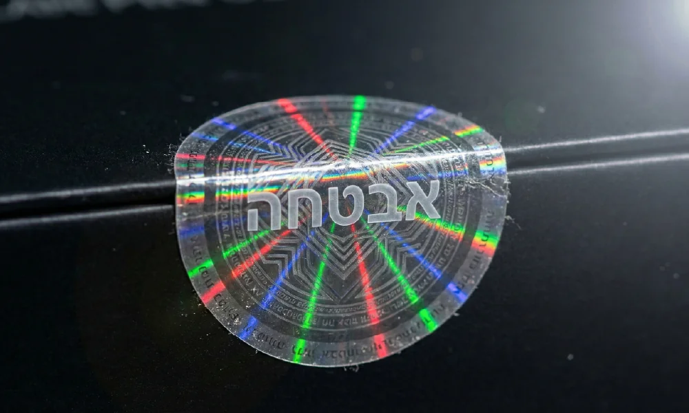 מדבקת הולוגרמה מנצנצת עם הכיתוב "אבטחה" על גבי מארז שחור, מייצגת פתרונות הגנה ומניעת זיופים.